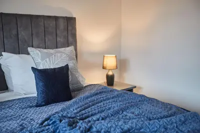 a bed with a blue comforter and pillows at Elfleda Stay - Modern 5 bedroom house with parking in Cambridge