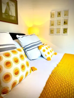 a bed with yellow and blue pillows on it at Gorgeous Comfy Cottage Walking Birdwatching Paddle Boarding and Seafood on the Doorstep in West Mersea