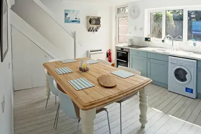 a kitchen with a wooden table with chairs and a washing machine at Gorgeous Comfy Cottage Walking Birdwatching Paddle Boarding and Seafood on the Doorstep in West Mersea