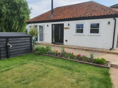 a white house with a black door and some flowers at River Cottage in Stoke Ferry