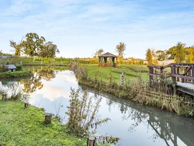 a river with a gazebo next to a field at Bear House- Uk45704 in Brinkley
