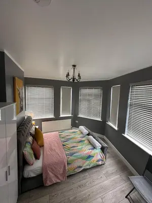 a bedroom with a bed and a chandelier and windows at Herbies Stay in Southend-on-Sea