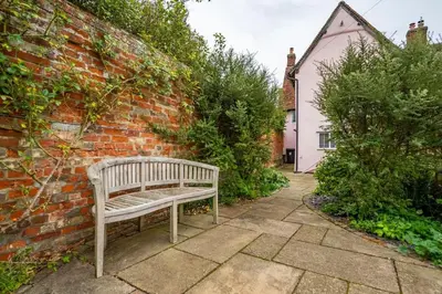 a wooden bench sitting next to a brick wall at Dragonfly Cottage, Long Melford in Long Melford