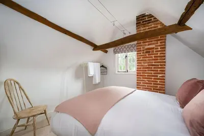 a bedroom with a white bed and a chair at Dragonfly Cottage, Long Melford in Long Melford