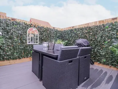 a patio with a black table and a hedge at Little Haven in Frinton-on-Sea