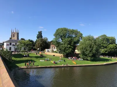 a group of people sitting on the grass next to a river at Cambridge Narrowboats - Beautiful Narrowboat Glyndwr in Cambridge
