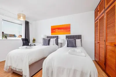 two beds in a bedroom with white walls and wood floors at 4 Bedroom House with Parking & Garden by Cherry Inn Short Let's & Services Accomodation in Cambridge