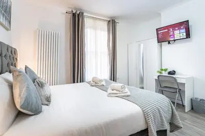 a bedroom with a white bed with a tv on the wall at Prestige Guest House Cambridge Modern Ensuite Rooms in Cambridge