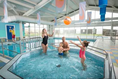 a woman and two children playing with a ball in a swimming pool at 3 BR - Luxury Family Home Near The Beach in East Mersea