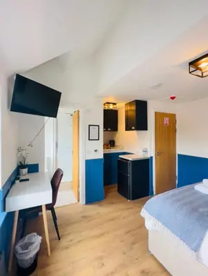 a bedroom with a bed and a desk and a kitchen at Sun Guest House Cambridge in Cambridge