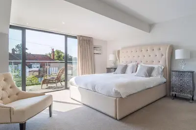 a white bedroom with a large bed and a chair at Luxurious resort house near beach - Mallards in Thorpeness