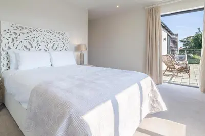 a white bedroom with a large bed and a balcony at Luxurious resort house near beach - Mallards in Thorpeness