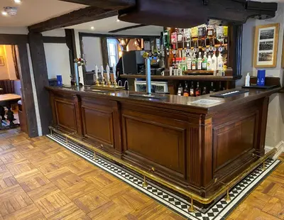 a large wooden bar in a pub with a counter at The Bull Inn in Woodbridge