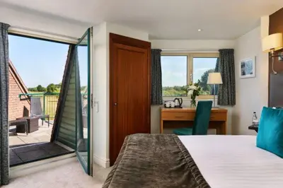 a bedroom with a bed and a desk and a balcony at Ufford Park Resort in Woodbridge