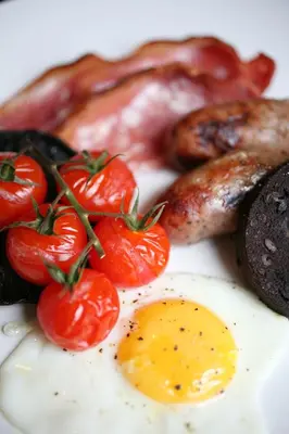 a plate of breakfast food with eggs sausage and tomatoes at The Crown Hotel in Woodbridge