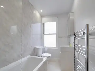 a white bathroom with a tub and a toilet and a window at Pass the Keys Modern and Spacious Terrace in Central Cambridge in Cambridge
