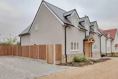 a white house with a fence in front of it at Kestrel Gardens Dunmow in Great Dunmow