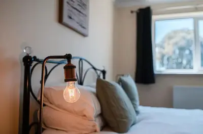 a light on a bed with pillows and a window at Spacious & Elegant 3BR Home Near Ipswich City Centre in Ipswich