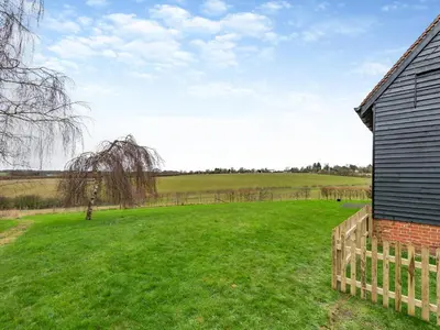 a field next to a house with a fence at Oak Cottage in Ware
