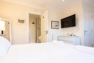 a white bedroom with a bed and a flat screen tv at Fromus Rise, Saxmundham in Saxmundham