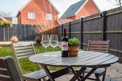a wooden table with two wine glasses and a bottle of wine at 4 Bed, 3 Bath in Colchester - Business, Contractor and Leisure - Singles or Superkings - Disc0unts in Colchester