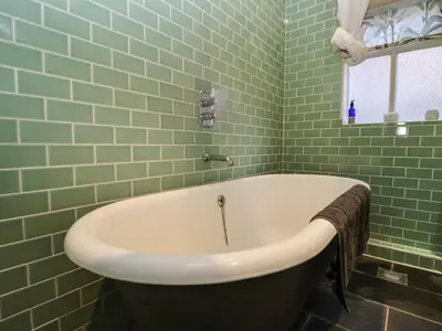 a bath tub in a green tiled bathroom with a window at 11a Market Cross Place in Aldeburgh