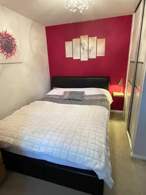 a bedroom with a bed with a red wall at Beautiful Peaceful Studio Flat in Waltham Abbey