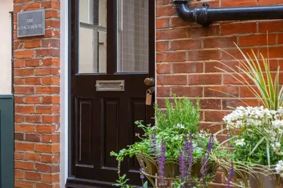 a black door to a brick house with flowers at Stylish and homely 1 bed Edwardian Coach House in Colchester
