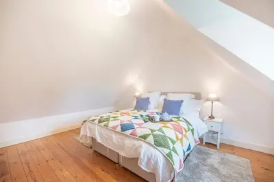 a white bedroom with a bed with a colorful comforter at 3 Old School Cottages, Wissett in Halesworth