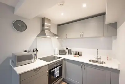 a kitchen with white cabinets and a clock on the wall at Modern,central 1 bedroom flat in Brentwood