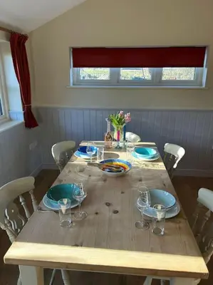 a wooden table with plates and wine glasses on it at A family and dog friendly haven, The Hayloft. in Saxmundham