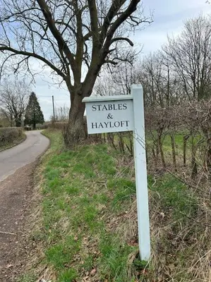 a white sign in the grass next to a road at A family and dog friendly haven, The Hayloft. in Saxmundham