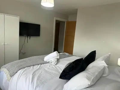 a white bed with black pillows on top of it at Spacious, bright 2 bed flat with 1 S/king bed. in Brentwood