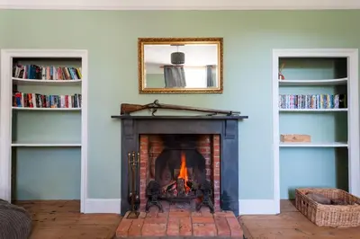 a fireplace in a living room with a mirror and books at FIRS Sleeps 15 Stunning country house with hot tub in Sudbourne