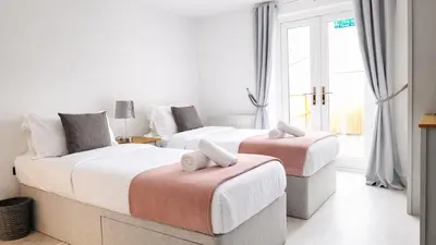 two beds in a hotel room with white walls and windows at Cambridge - Modern 4-BR Home with Gardens & Wi-Fi in Cambridge