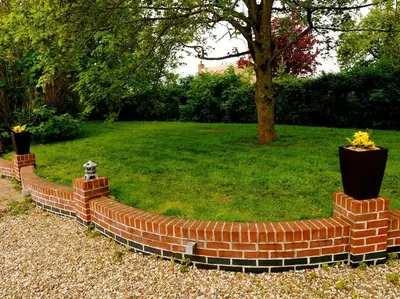 a brick retaining wall with flowers in a yard at Deluxe 1 Bed Versace Hot Tub Sky TV Cinema Screen in Great Sampford
