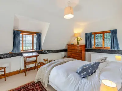 a bedroom with a bed and a desk and windows at Malting Cottage in Much Hadham