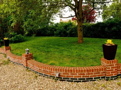a brick retaining wall with flowers in a yard at Deluxe 1 Bed Versace HotTub SkyTV in Saffron Walden