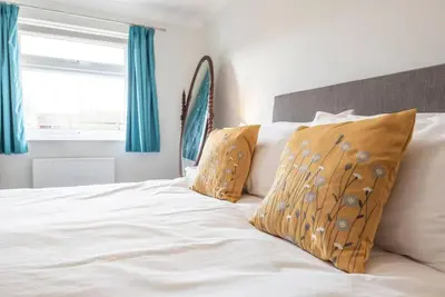 a bed with white sheets and pillows with blue curtains at 111 Front Street, Orford in Woodbridge