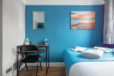 a bedroom with a blue wall with a bed and a desk at Welcome to Northview House Stylish 4 Bedroom Home in Southend by Jesswood Properties Contractors Corporates Relocation Stays Long Stays Welcome in Southend-on-Sea