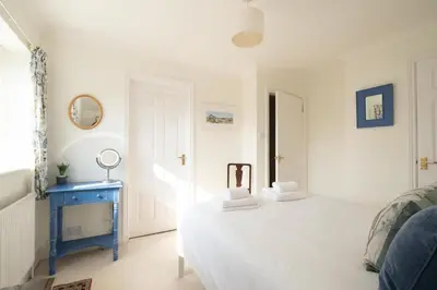 a white bedroom with a bed and a blue table at Harvest Cottage in Aldeburgh