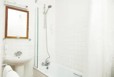 a white bathroom with a shower and a sink at White Hart Hotel by Greene King Inns in Braintree