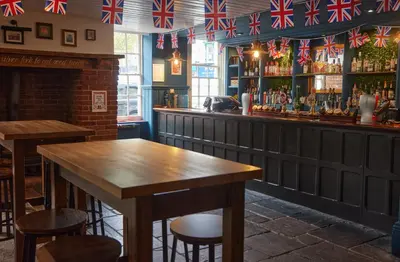 a bar with a wooden table and some flags at White Hart Hotel by Greene King Inns in Braintree