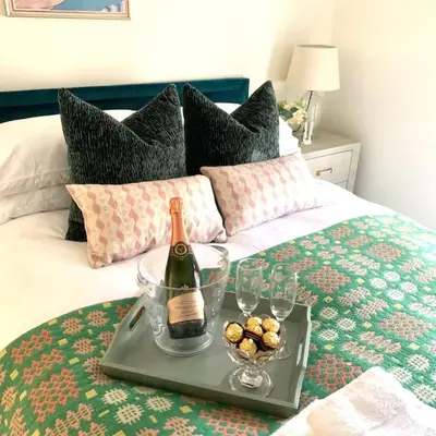a tray with a bottle of wine and glasses on a bed at The Yellow cottage on the hill. in Framlingham
