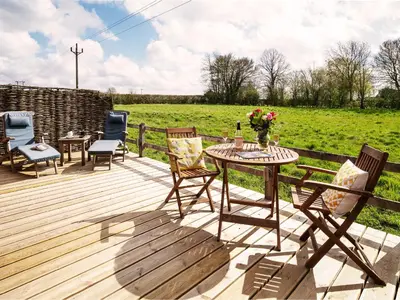 a wooden deck with a table and chairs and a field at The Workshop by The Suffolk Cottage Collection in Bruisyard