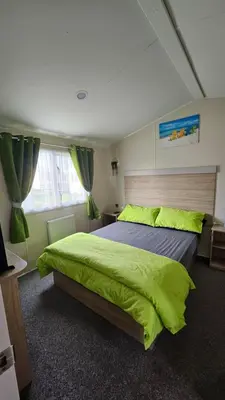 a bedroom with a large bed with a green blanket at Pura Vida Caravan in Saint Osyth