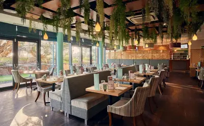 a restaurant with wooden tables and chairs and windows at Wivenhoe House Hotel in Colchester