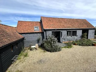 a black house with a red roof and a yard at Mersea best kept secret in Colchester
