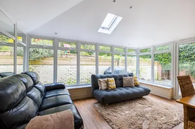 a living room with leather furniture and large windows at En-suite with double bed on mezzanine and desk in family home in Hertford