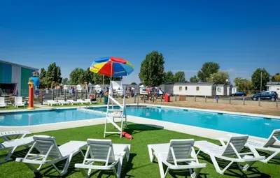 a group of chairs and an umbrella next to a swimming pool at Caravan at Seawick Holiday Park Close to Beach in Saint Osyth